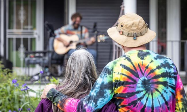 A couple watches a performer play from a front porch at Cooper Young Porchfest.
