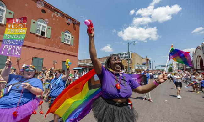 People march down Beale Street with rainbow flags and signs as part of the Memphis Pride Parade.