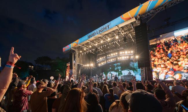 Crowd watching a performer on stage at night at RiverBeat Music Festival.