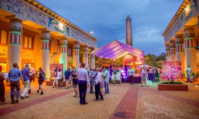 Guests gathered inside Memphis Zoo with neon lights illuminating tents and structures in the background for Zoo Rendezvous.