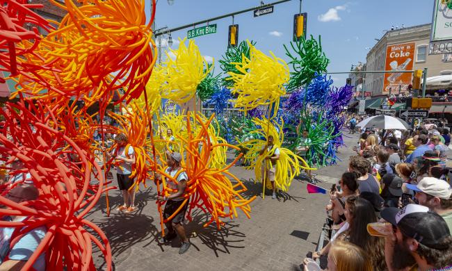 People marching in Pride Parade with large colored balloon outfits in colors of the rainbow