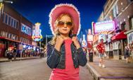 A young girl dressed in a pink hat and Elvis-inspired sunglasses stands on Beale Street in Memphis, Tennessee.