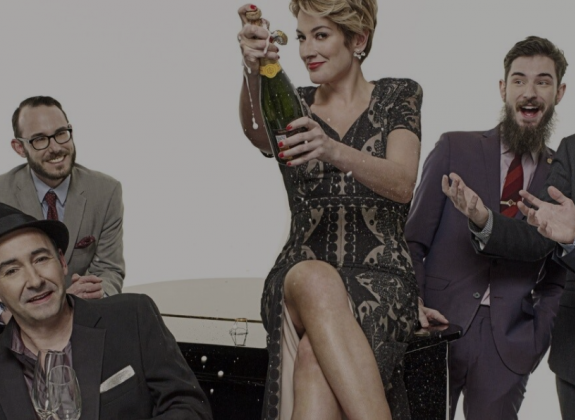 The Hot Sardines band popping a bottle of champagne on top of a piano