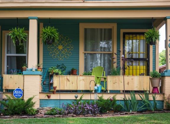 Front porch with hanging plants and a yellow door