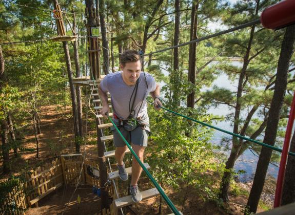 man climbs across treetop bridge