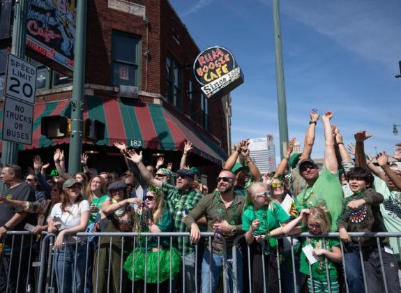 crowd of people dressed in green shirts and green beads all standing in a crowd with their hands up at the beale street parade