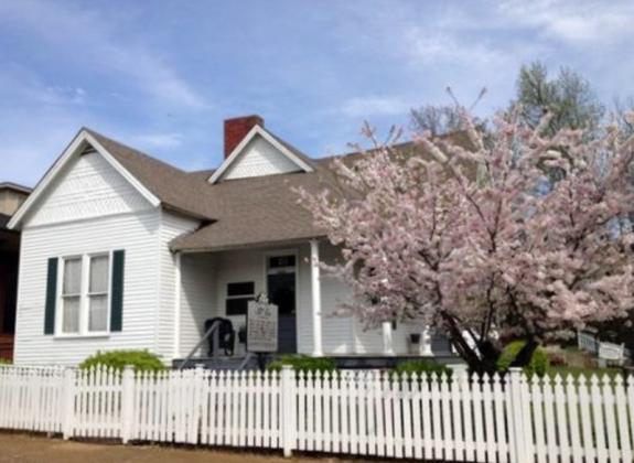 Wooden small house with a picket fence and small tree with blooms in front Photo 3