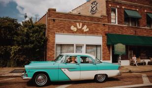 Vintage blue car parked in front of sun studio.