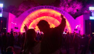 Couple listens to a concert at Overton Park Shell, which is illuminated in pink and orange neon lights.