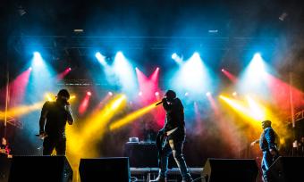 stage at concert with yellow, blue, red lights and artists on stage