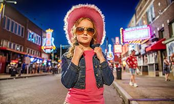 A young girl dressed in a pink hat and Elvis-inspired sunglasses stands on Beale Street in Memphis, Tennessee.