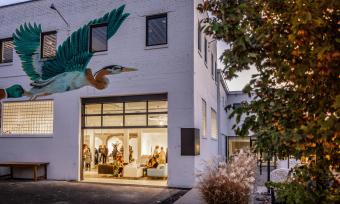 People inside the gallery space at Ugly Art Co with a large blueish-green bird mural above the entrance.